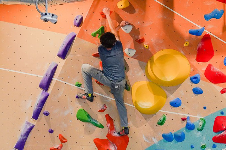 An individual at a wall climbing gym, mid-climb.